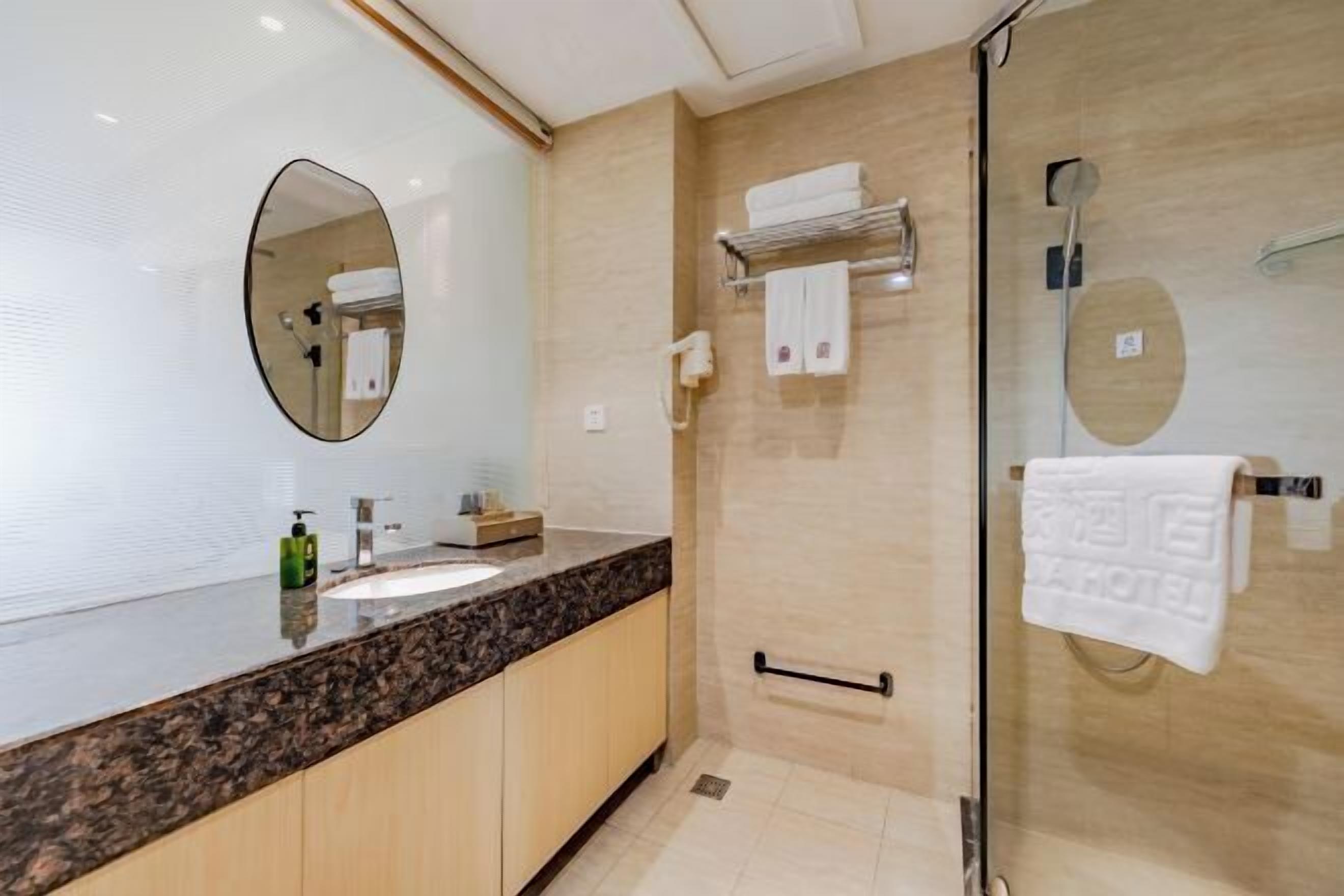 Un baño moderno con encimera de granito, un espejo ovalado grande, cabina de ducha de vidrio y un perchero para toallas.