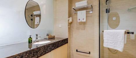 A modern bathroom with a granite countertop, a large oval mirror, a glass shower enclosure, and a towel rack.