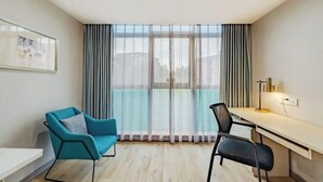 Egy modern szoba, amelyben van egy íróasztal, két szék, egy nagy ablak, amelyen függöny van, és egy kép, amely keretben van a falon.