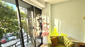 A living room with a green sofa, a glass door leading outside, and a view of a street with cars and trees. - Charming, fully appointed 1-bedroom apartment in PV’s amazing Zona Romantica (Puerto Vallarta)