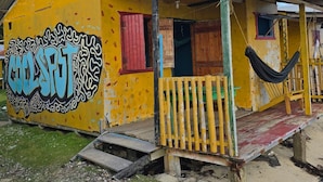 A yellow building with graffiti, a porch, and a hammock. - Graces Place Cool Spot  (Corn Islands)
