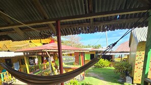 A hammock on a wooden deck overlooking a colorful courtyard with a sign that reads "ALCHA". - Graces Place Cool Spot  (Corn Islands)