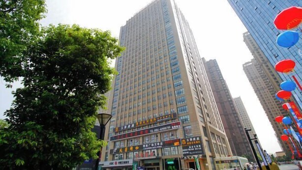 Un edificio alto con varios pisos, grandes ventanales y diversos letreros y anuncios en la planta baja.