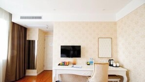 Habitación de hotel con un escritorio blanco, un televisor, una silla y una mesita con hervidor y tazas.