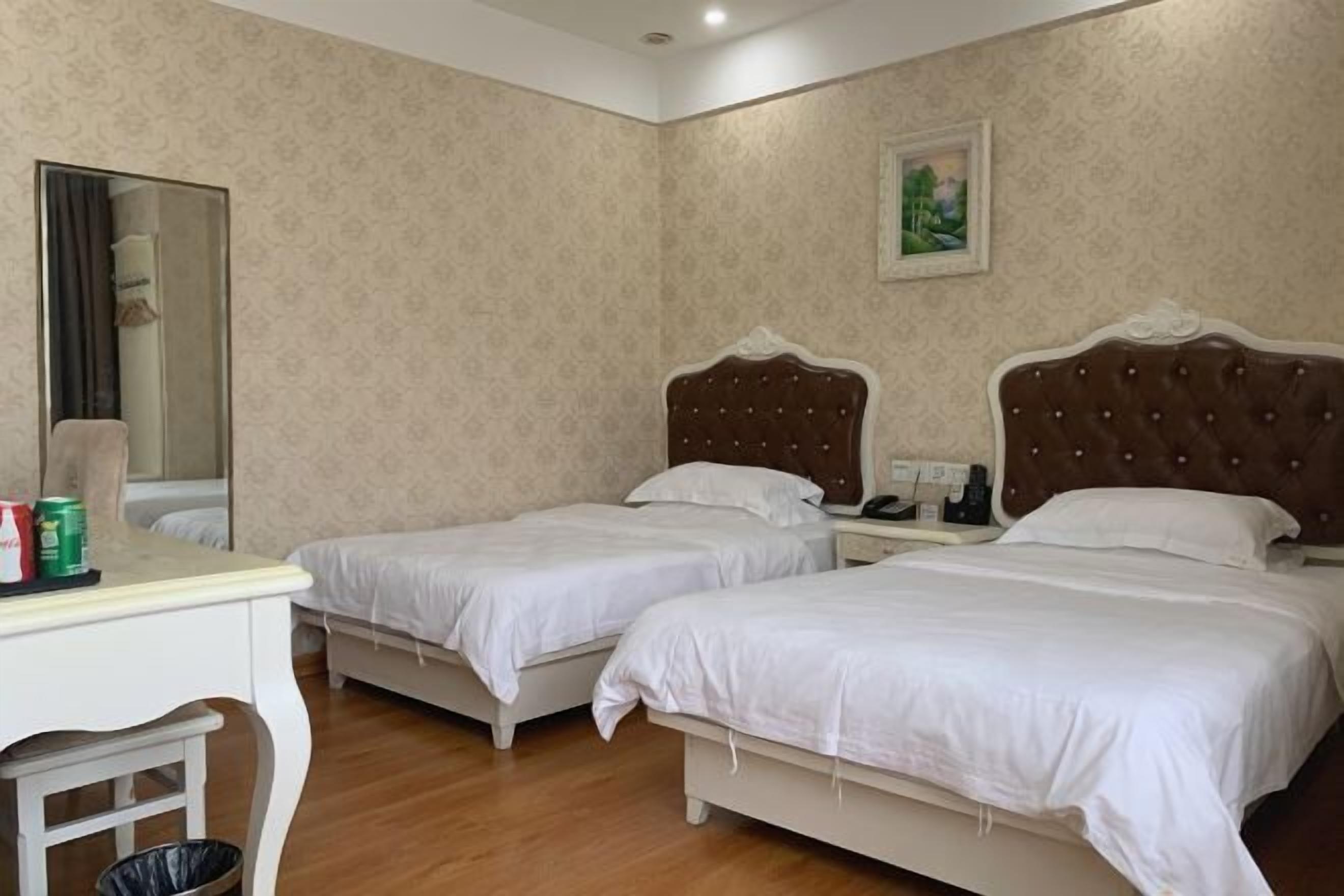 A hotel room with two beds, a desk, a chair, a trash bin, and a painting on the wall.