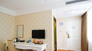 Una habitación de hotel con un escritorio blanco, televisión, una silla, un cubo de basura y una puerta.