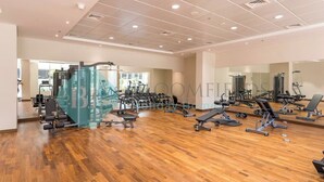 A spacious gym with various exercise equipment, large mirrors, and a wooden floor. - Bloomfields Luxurious 1BR Down Town (Dubai)