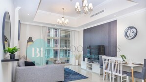 A modern living room with a sofa, dining table, chairs, and a TV. - Bloomfields Luxurious 1BR Down Town (Dubai)