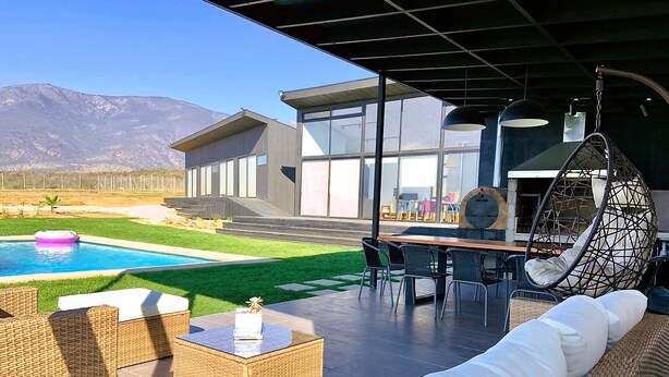 Une terrasse extérieure moderne, dotée de meubles en osier, d’une piscine et d’un fauteuil suspendu.