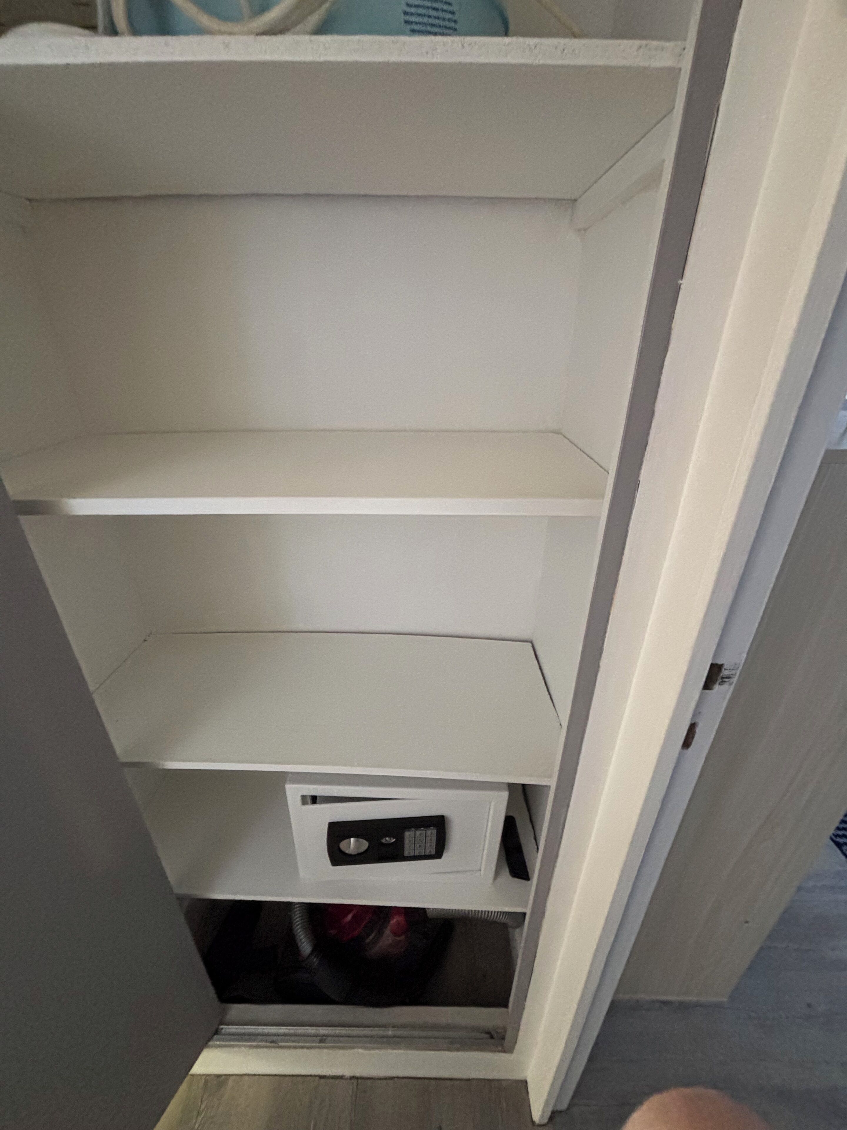 Een witte kast met drie vakken, waarvan één een zwart elektronisch apparaat bevat.