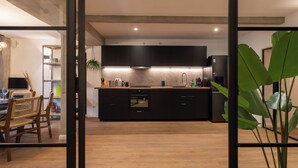 A modern kitchen with dark cabinets, a central island, and a dining area with wicker chairs. - Urban Wave Apartment I (Hamburg)
