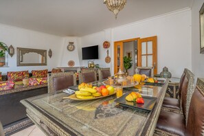 Un espace repas avec une table en verre, des chaises et une variété de fruits et de boissons.