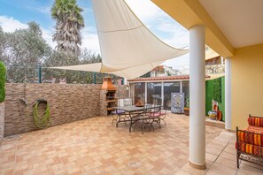 Une terrasse extérieure avec une table et des chaises, un barbecue et un grand parasol pour faire de l’ombre.