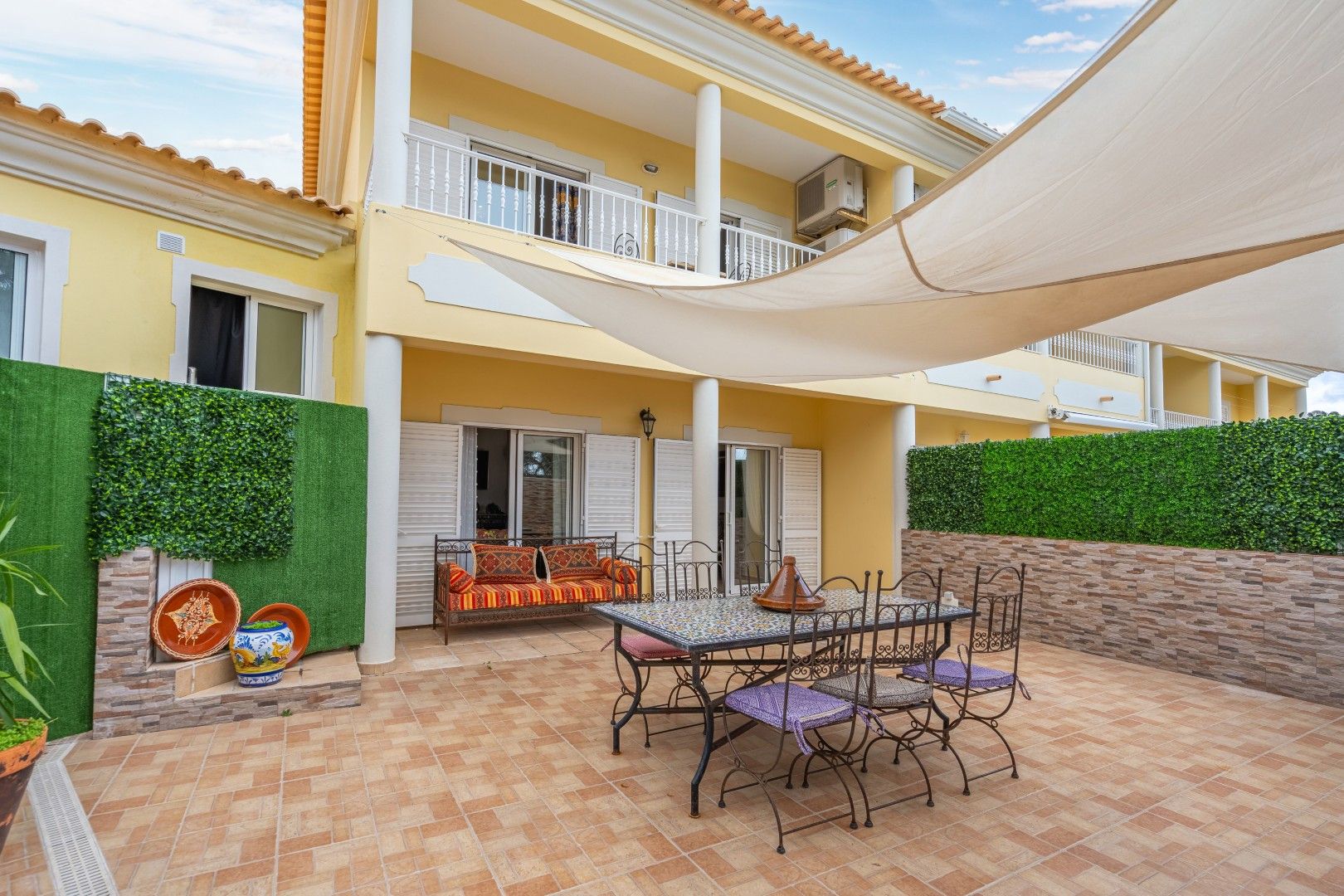 A two-story building with a patio area featuring a table and chairs, a sofa, and a decorative wall.