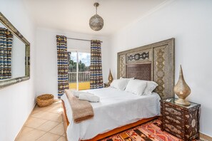 Une chambre à coucher avec un lit, une table de chevet, une lampe, une fenêtre avec des rideaux et un mur à motifs.