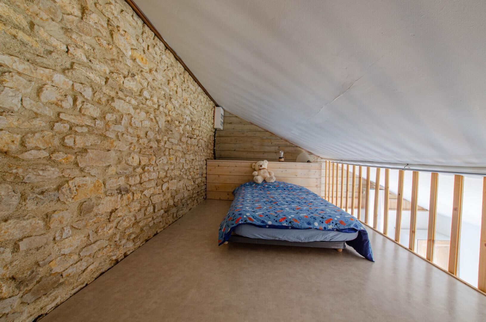 Une chambre avec un mur en pierre, un lit en bois et une vue sur l’extérieur depuis un balcon.