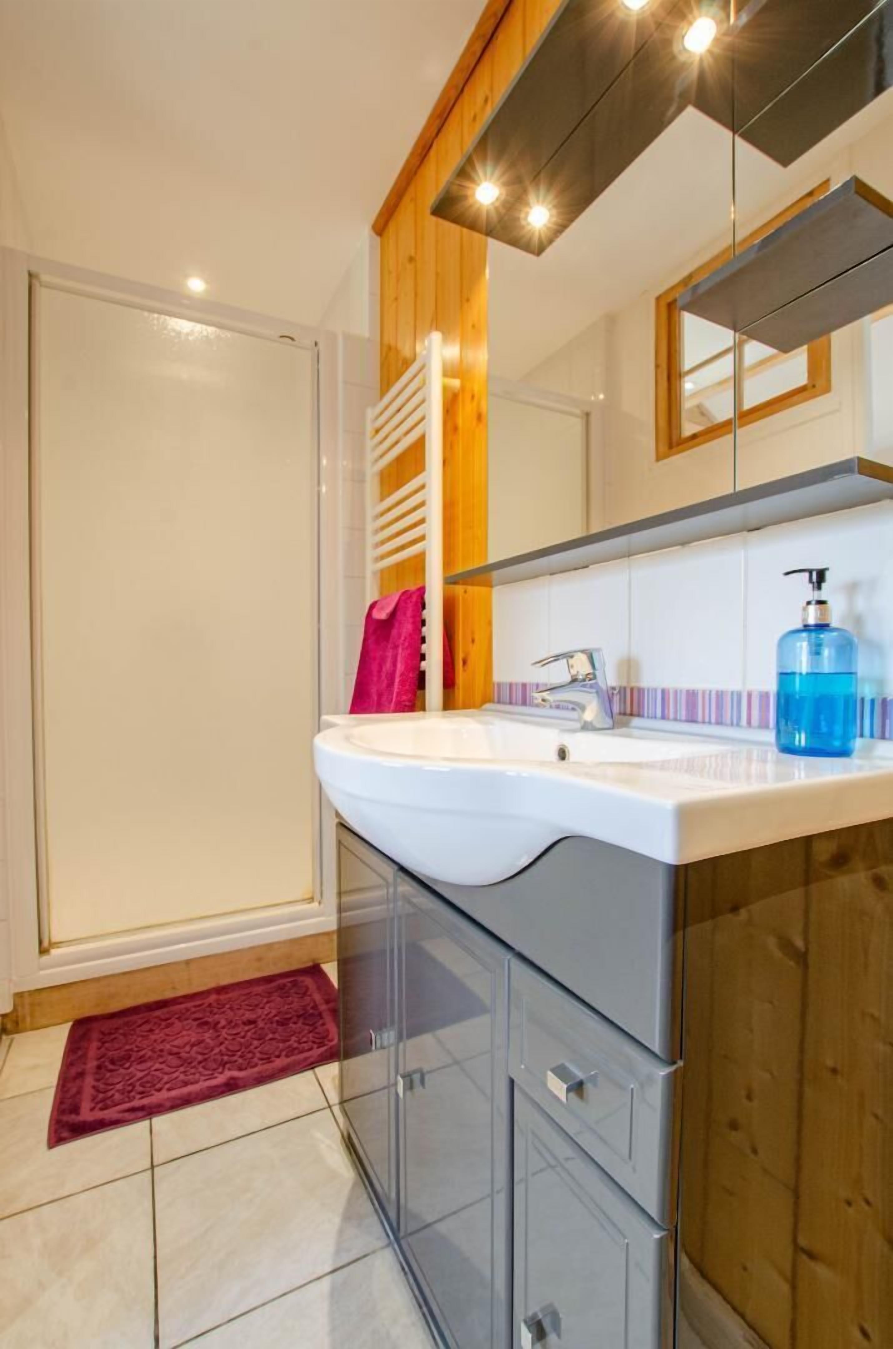A modern bathroom with a glass shower enclosure, a white sink with a mirror above it, and wooden cabinetry.