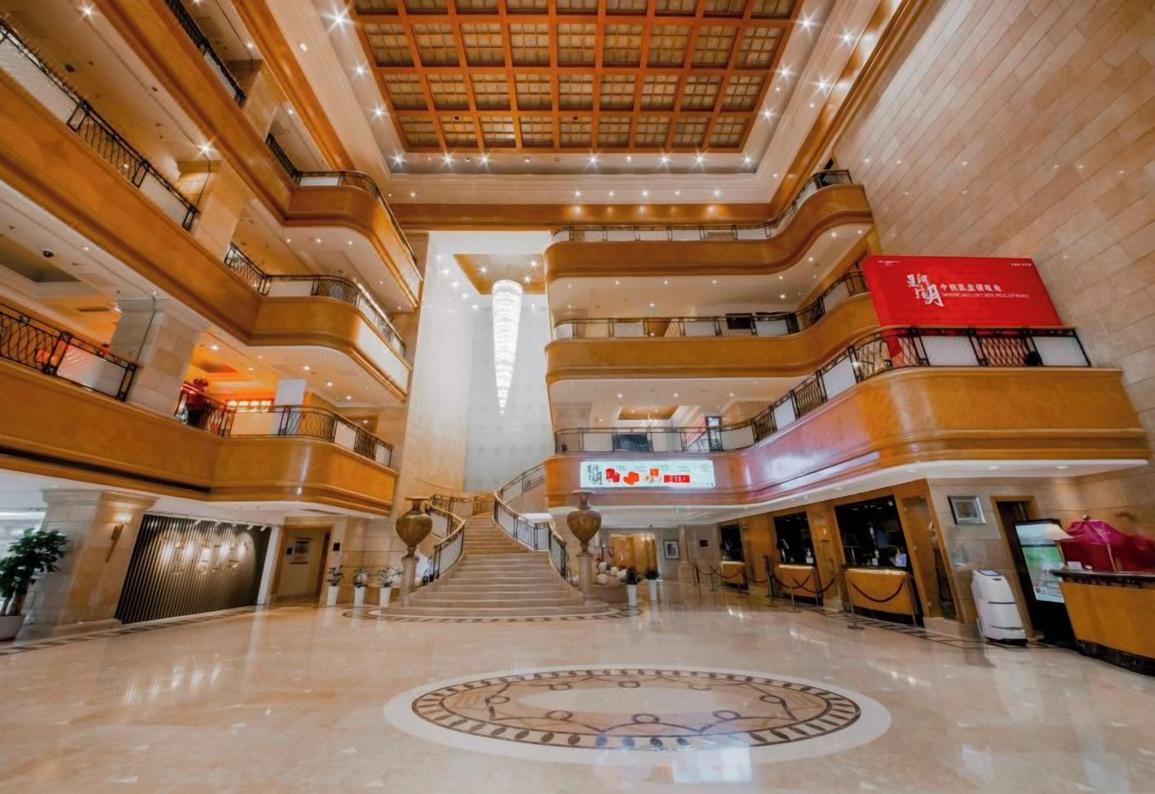 Um hall de hotel em vários níveis, com uma escadaria imponente, várias varandas e um grande balcão de recepção.