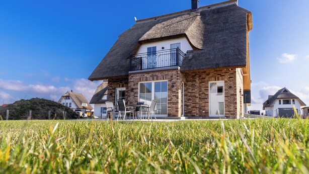 Ein zweistöckiges Haus mit einem Strohdach, einem Balkon und Blick auf ein grasbewachsenes Feld.