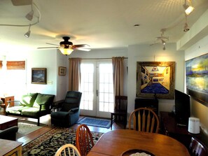 A living room with a dining table, chairs, a sofa, a ceiling fan, and a painting on the wall.