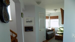 Ein Flur mit einer Holztreppe, einer Tür, einem gerahmten Bild, einem grünen Sofa und einem Fenster mit Jalousien.