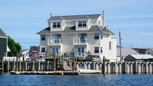 Ein mehrstöckiges Haus mit einer Anlegestelle, die sich ins Wasser erstreckt, mit einem Boot und einem geparkten Auto in der Nähe.