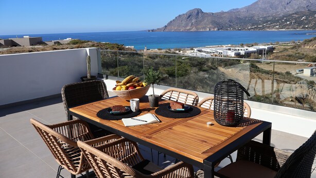 A wooden table with wicker chairs on a balcony overlooking a coastal view with mountains in the distance. - One Luxury House 
Above The Sea .... (Myrthianos Plakias)