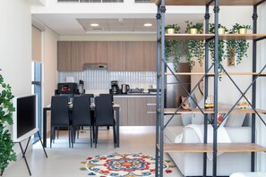 A modern kitchen with wooden cabinets, a dining area with black chairs, a coffee machine, and a TV. There is a staircase with a metal railing and shelves with plants. - Bloomfields Artistic STU in The View (Abu Dhabi)