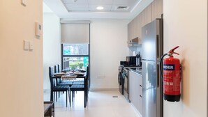 Une cuisine moderne équipée d’appareils électroménagers en acier inoxydable, un coin repas avec des chaises noires et un extincteur fixé au mur.