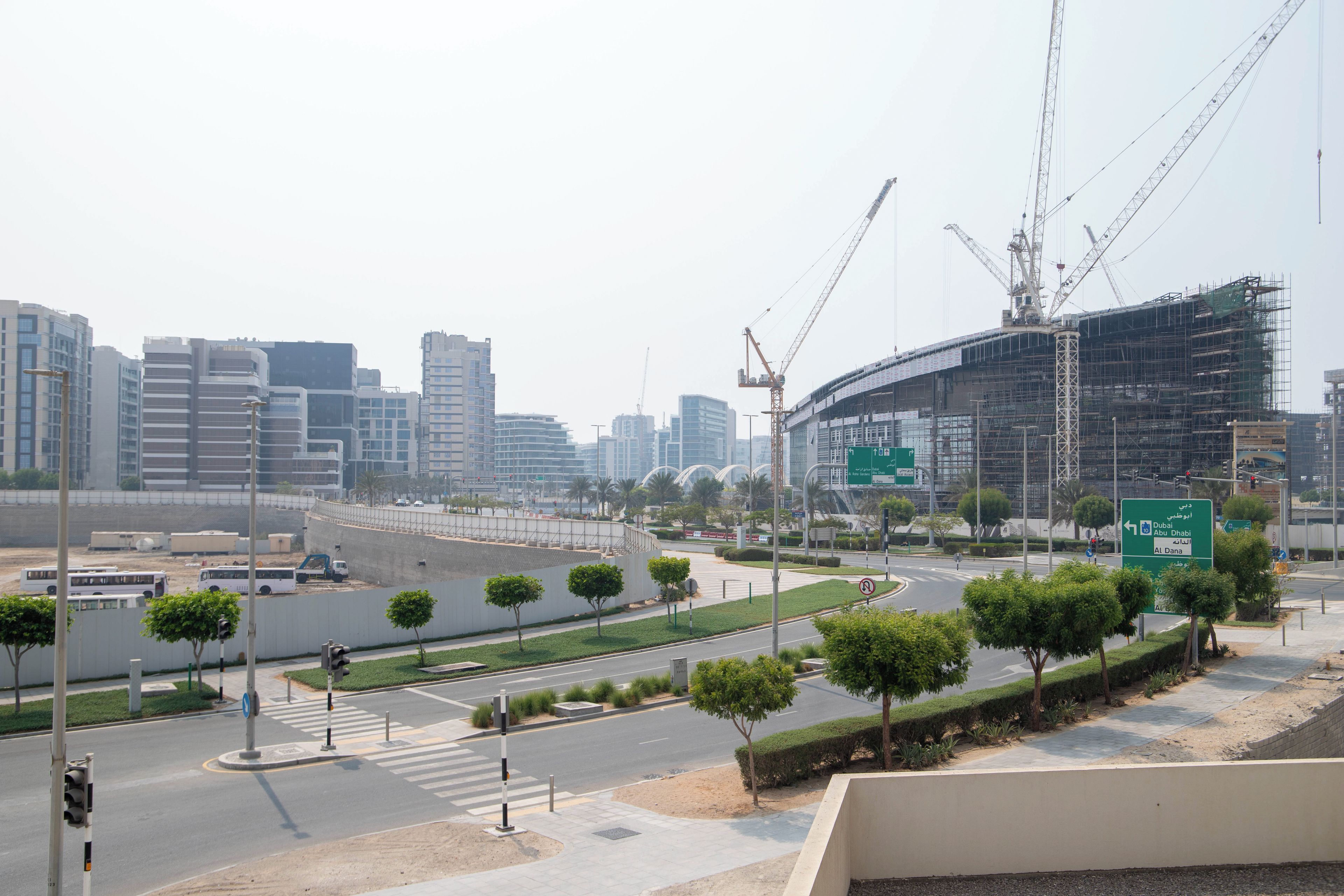 Paisagem urbana com edifícios modernos, um canteiro de obras e uma rua com semáforos.