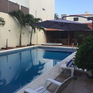 Une piscine dotée d’un parasol, de chaises longues et de palmiers.