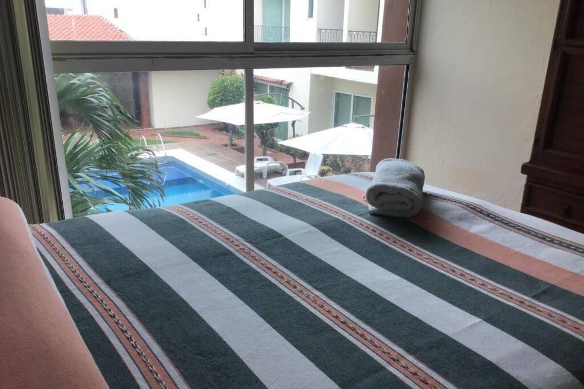 A hotel room with a bed, a window, and a view of a swimming pool and outdoor seating area.