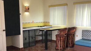 Une cuisine compacte avec un coin repas, comprenant un sol carrelé, une table à manger, des chaises et un canapé agrémenté d’un coussin à motifs.