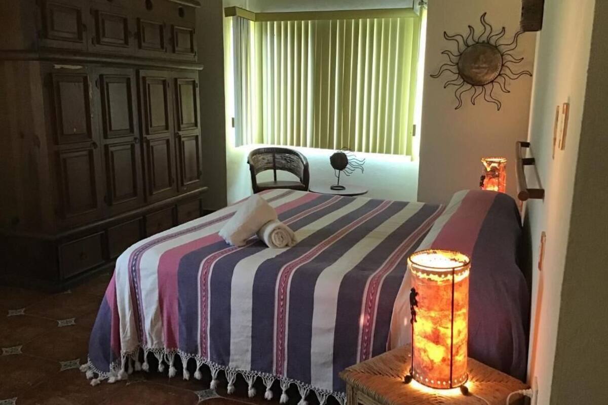 A bedroom with a bed, a bedside lamp, a chair, and a window with blinds.