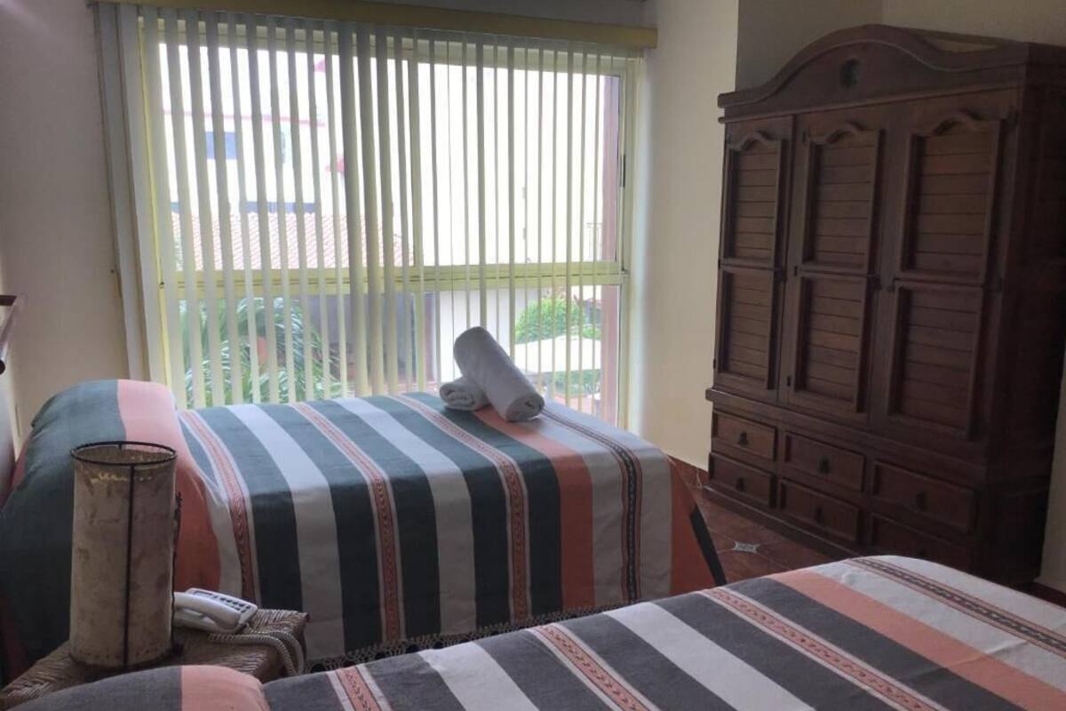 A room with two beds, a wooden wardrobe, and a window with blinds.