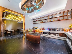A modern hotel lobby with a marble floor, a central island with food and drinks, a seating area, and a decorative ceiling light fixture. - Yitel (Chengdu)