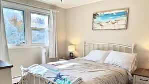 A bedroom with a bed, bedside tables, a lamp, a window with curtains, and a painting on the wall. - Cozy 2-bedroom, 1-bathroom condo,  two short blocks from the beach! (Old Orchard Beach)