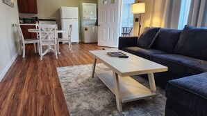 A compact living space with a dining area, a sofa, a coffee table, and a kitchen in the background.