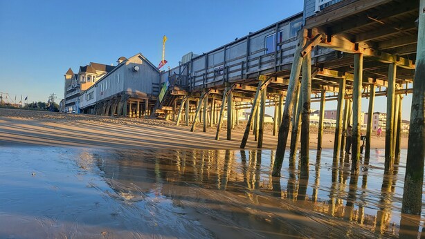 A pier with buildings on stilts, a sandy beach, and a clear sky.