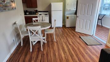 A compact kitchen with a dining area, wooden flooring, and a door leading to a balcony.