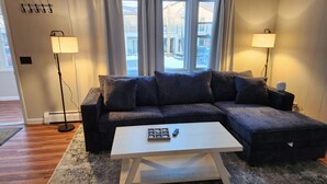A modern living room with a sectional sofa, a white coffee table, and two floor lamps. - Splendid, two-bedroom, one-bathroom condo,  two short blocks from the beach! (Old Orchard Beach)