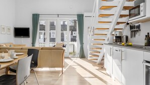 A modern kitchen with white cabinets, a built-in oven, and a coffee maker. There is a dining area with a table and chairs, and a sofa. - Cozy home in Vestervig with sauna (Vestervig)