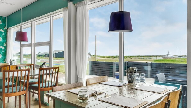 A dining area with a view of the beach and a boat. - Cozy home in Vestervig with sauna (Vestervig)