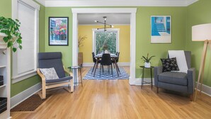 A living room with a dining area, green walls, wooden flooring, and modern furniture. - Charming Green Lake Craftsman – Hot Tub, AC, Dog Friendly, Walk to Lake & C... (Seattle)