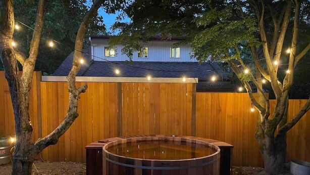 A hot tub in a backyard with a wooden fence and string lights. - Charming Green Lake Craftsman – Hot Tub, AC, Dog Friendly, Walk to Lake & C... (Seattle)