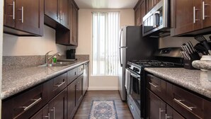 Une cuisine moderne avec des meubles en bois foncé, des plans de travail en granit, des appareils électroménagers en acier inoxydable et un îlot central.