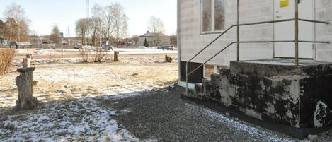 A building with a concrete staircase leading to a door, surrounded by a gravel area with sparse snow.