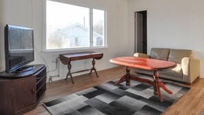 Een woonkamer met een televisie, een houten tafel, een bank en een raam met uitzicht op huizen.