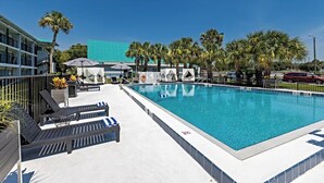 A swimming pool with lounge chairs and umbrellas, surrounded by palm trees and a building with a green roof. - Palm Tree Inn Altamonte Springs Orlando (Altamonte Springs)