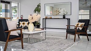 A modern living room with a black sofa, a coffee table, and two armchairs. There is a large mirror on the wall and a plant on the coffee table. - Palm Tree Inn Altamonte Springs Orlando (Altamonte Springs)